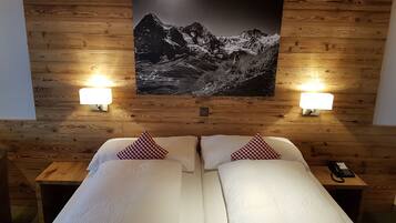 A hotel room with two beds, wooden walls, a mountain landscape painting, and bedside lamps.