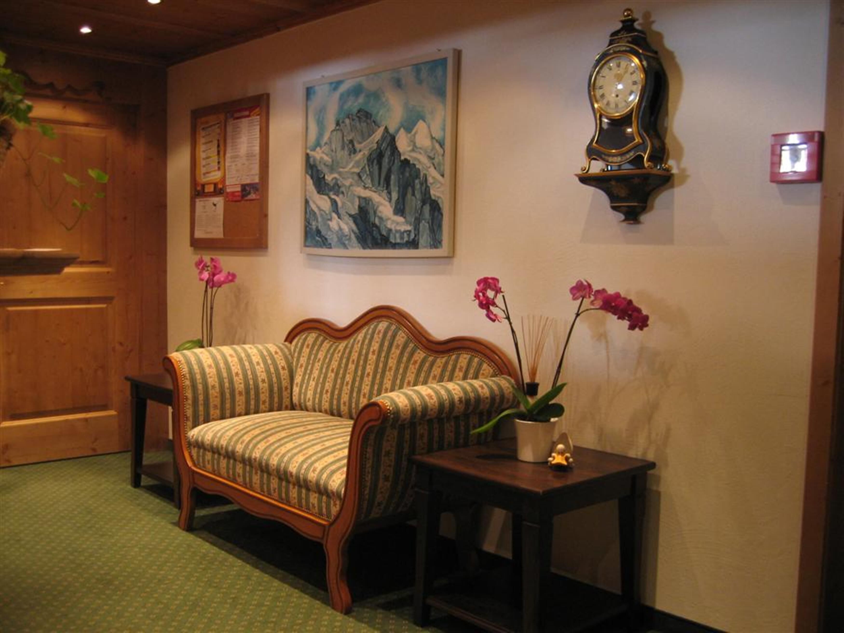 Una habitación acogedora con puerta de madera, un sofá estampado, una mesita con una orquídea en maceta, un reloj de pared y un cuadro enmarcado de montañas.