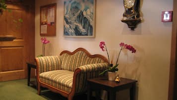 Una habitación acogedora con puerta de madera, un sofá estampado, una mesita con una orquídea en maceta, un reloj de pared y un cuadro enmarcado de montañas.