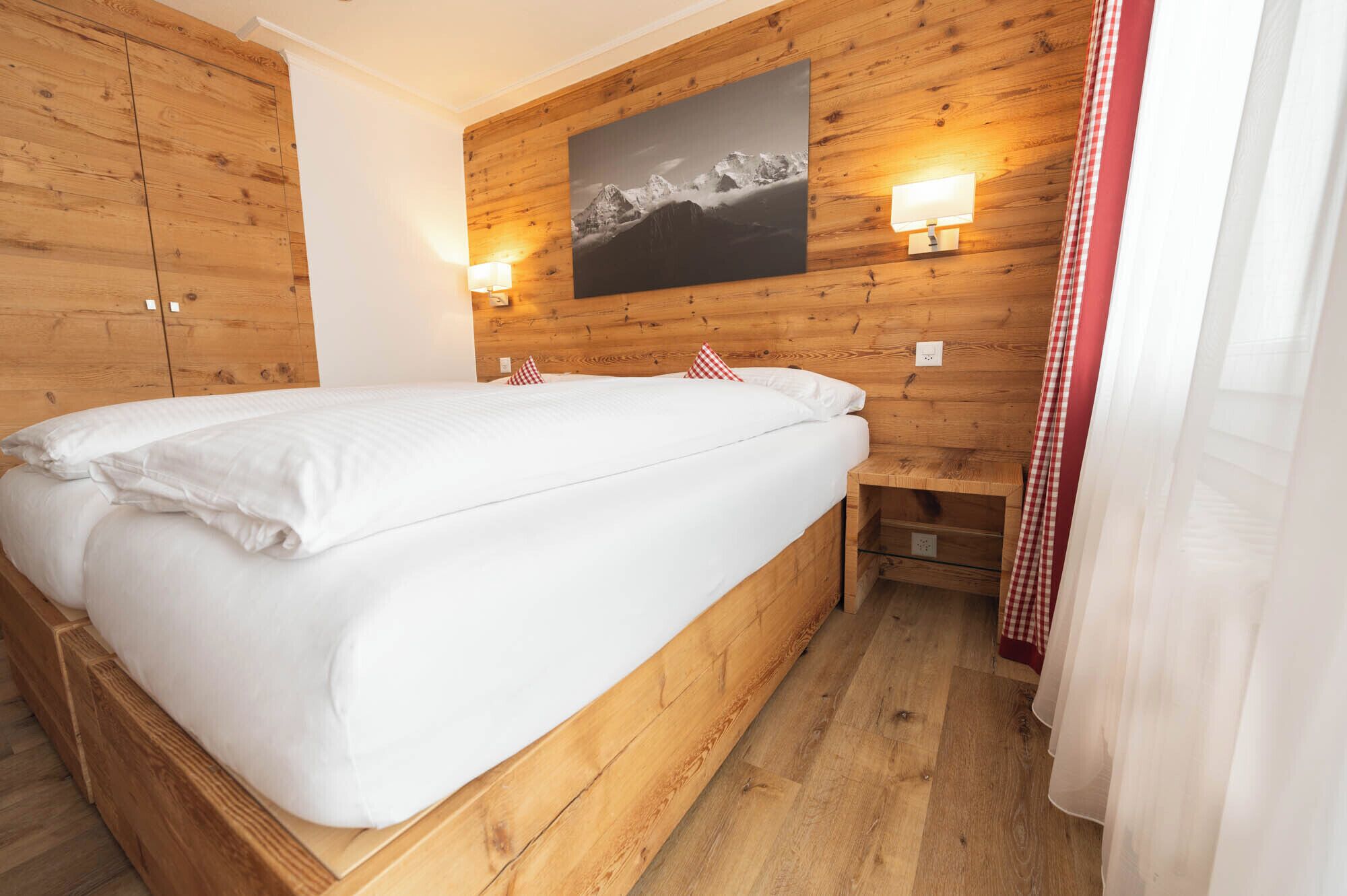 A wooden-paneled room with a bed, a wall-mounted lamp, and a painting of mountains.