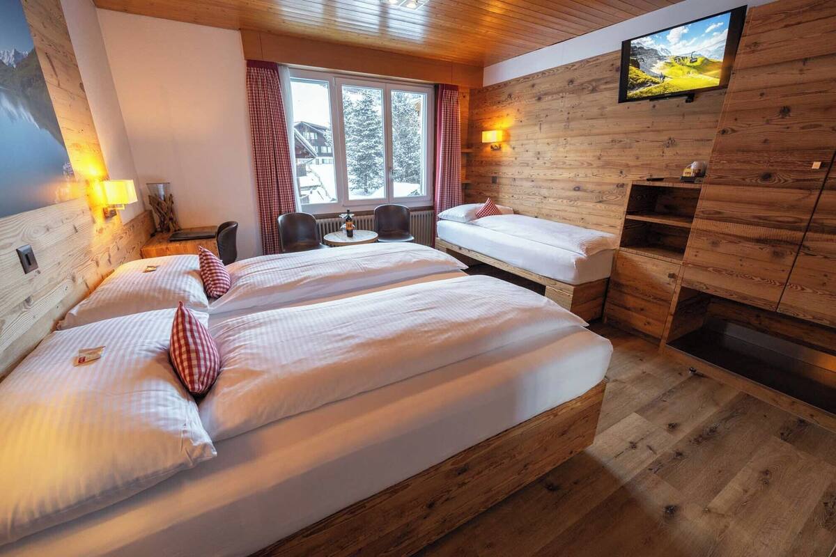 Habitación con dos camas, un televisor en la pared, una ventana con cortinas y decoración de madera.