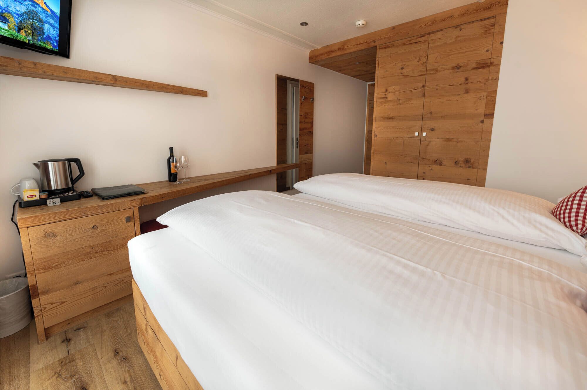 A bedroom with a wooden bed, a wooden desk with a kettle, a wine bottle, and glasses.