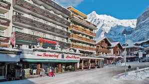 A hotel with multiple balconies, a ski resort sign, and a mountain backdrop. - Hotel Bernerhof Grindelwald (Grindelwald)
