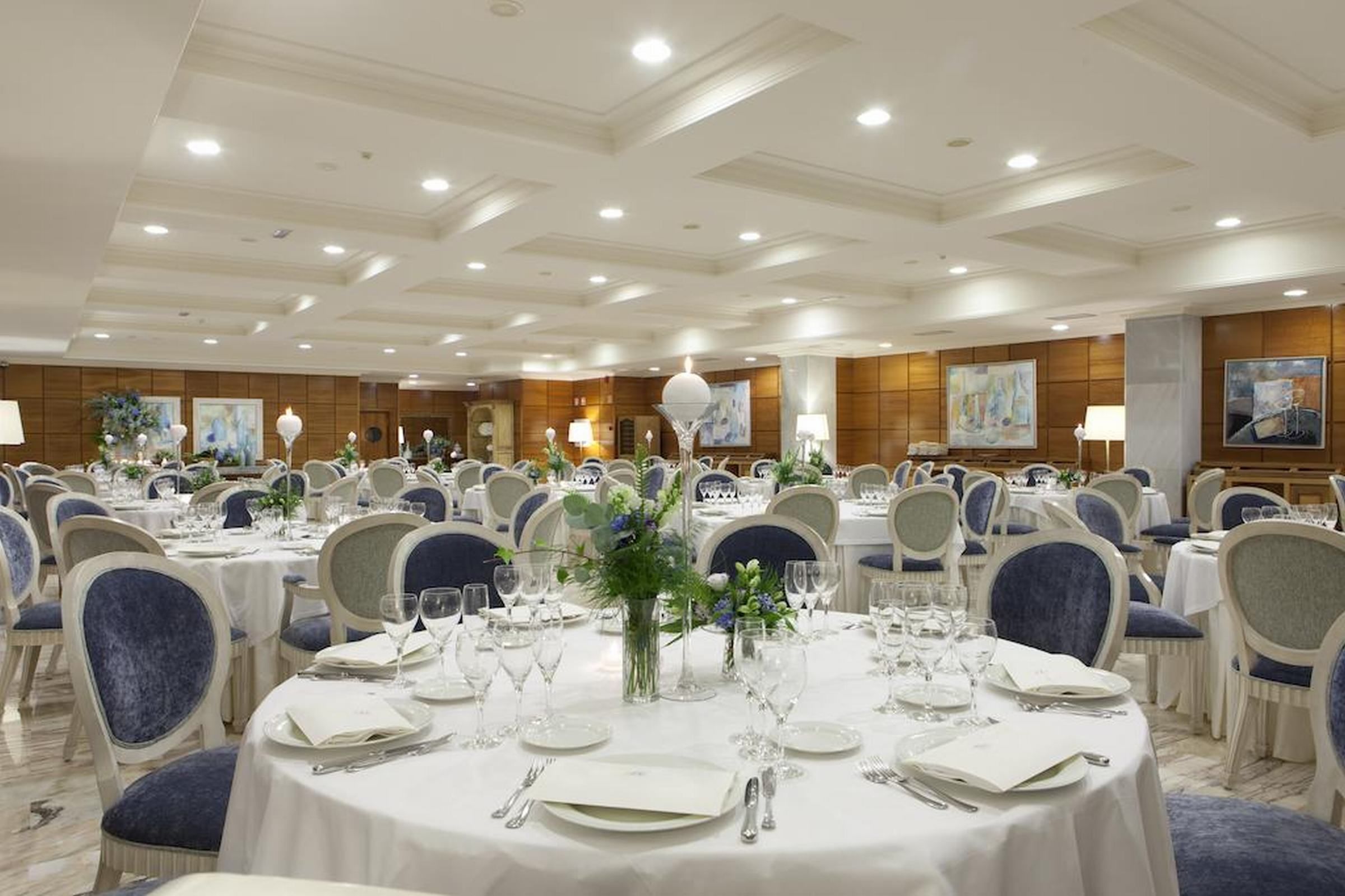 A banquet hall with round tables, chairs, and floral centerpieces.