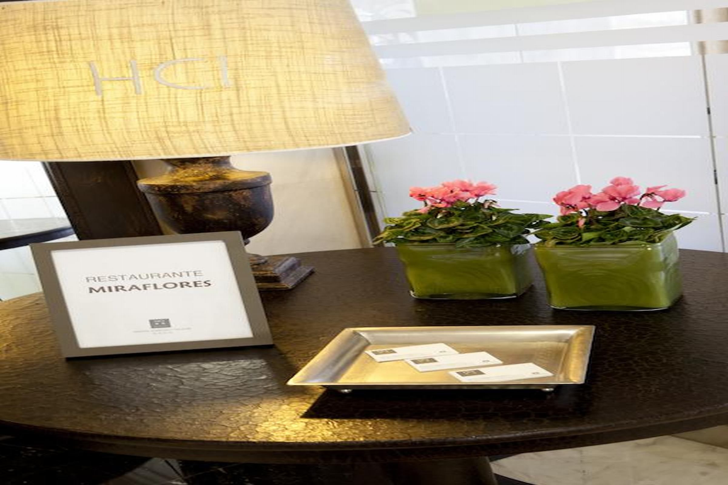 A table with a framed sign, a lamp, and two green vases with pink flowers.