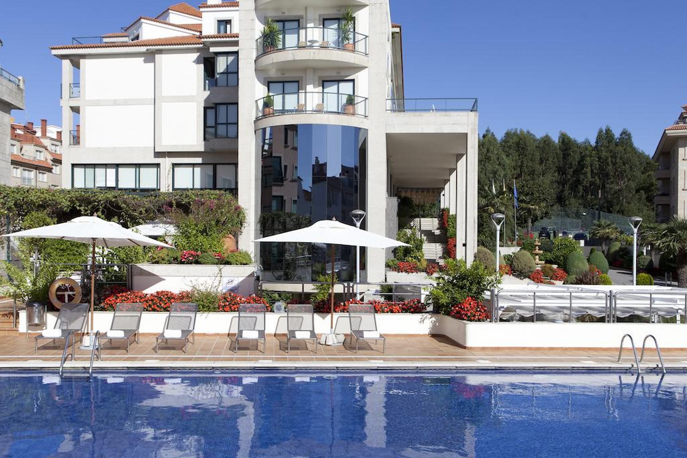 A modern building with a pool, lounge chairs, and umbrellas.
