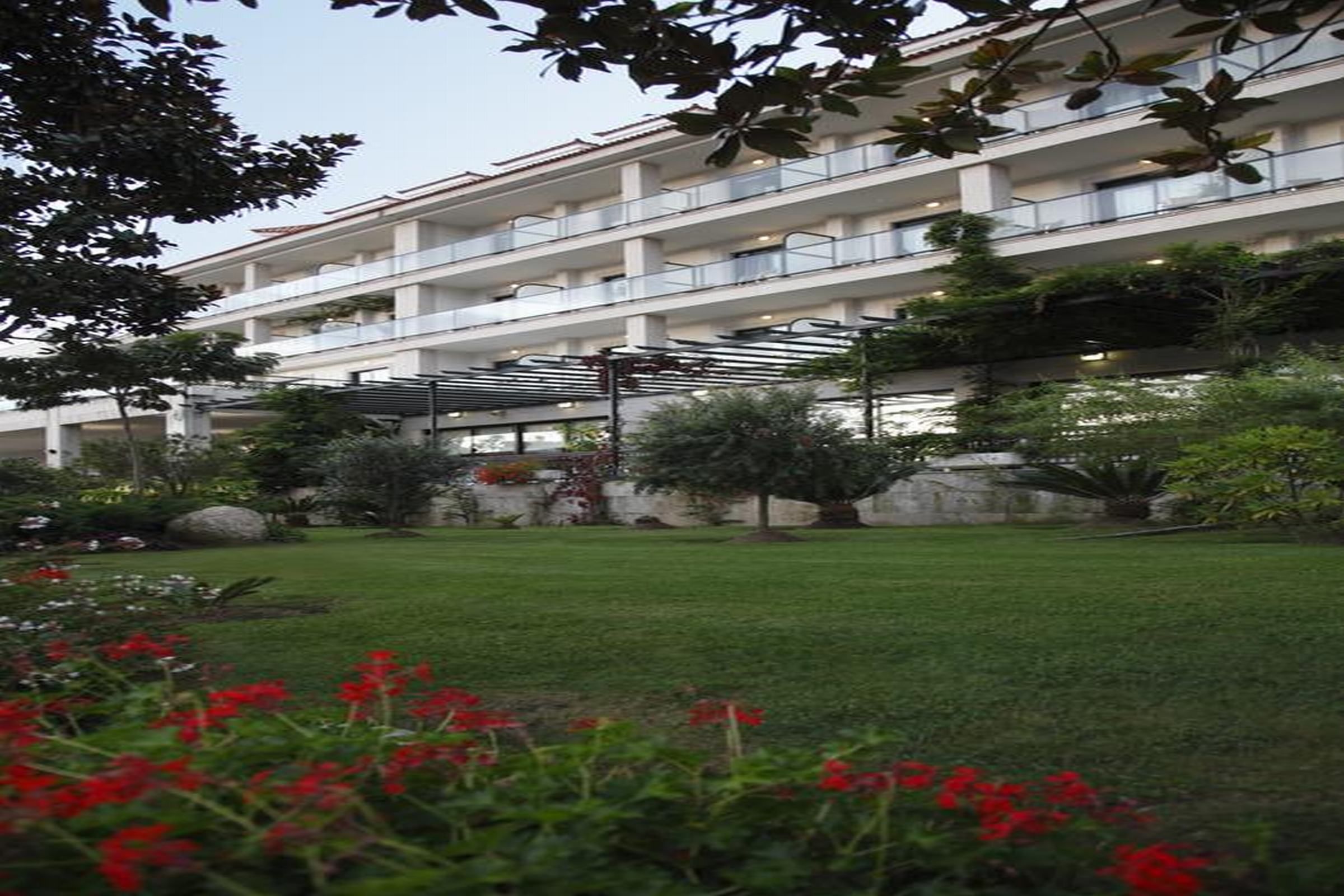 Un hotel de varios pisos con balcones y un jardín con flores rojas.