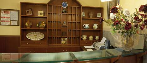 A reception area with a wooden reception desk, a glass counter, and a wall-mounted display of various ceramic items.