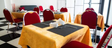A hotel dining area with tables set for four, red chairs, and a black and white checkered floor.