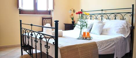 A neatly made bed with a tray of orange juice, a vase with flowers, and a bedside table with a lamp.