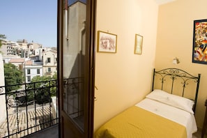 A room with a bed, a balcony with a view of buildings, and two framed pictures on the wall. - Hotel Columbia (Palermo)