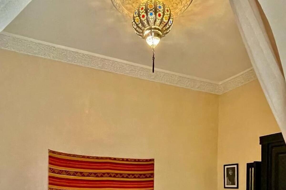 Una habitación de hotel con una cama, un cabecero estampado, una mesita de noche pequeña y una lámpara en el techo.