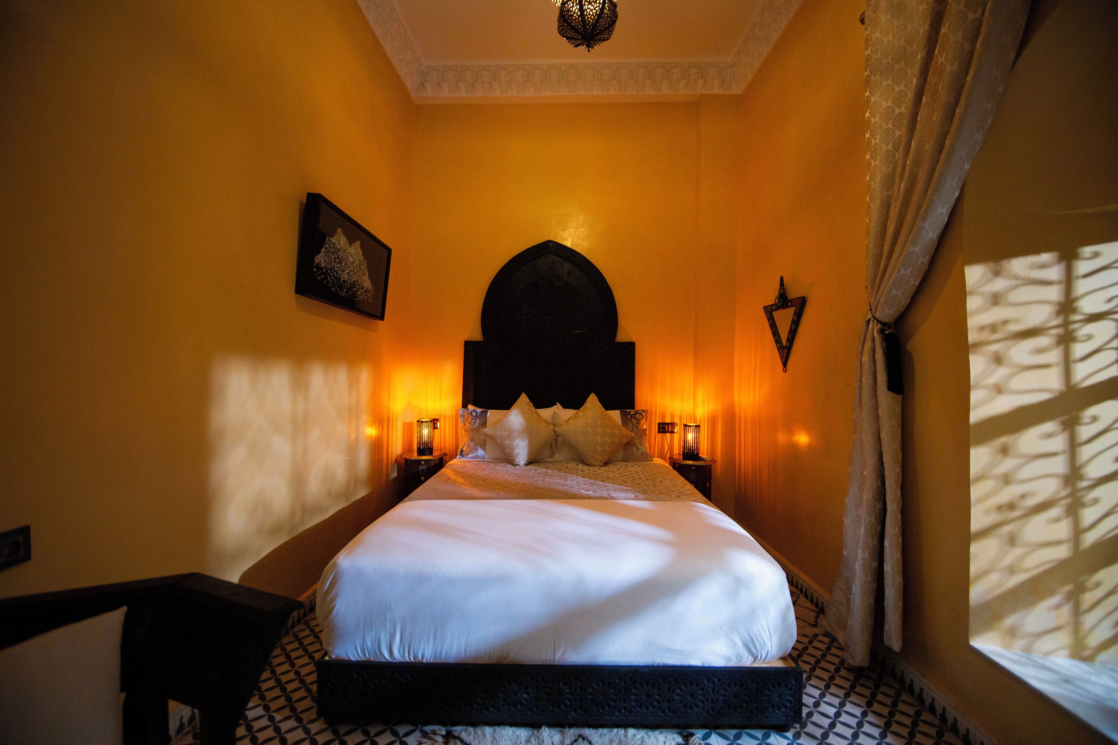 A bedroom with a large bed, a decorative ceiling light, and a window with patterned curtains.