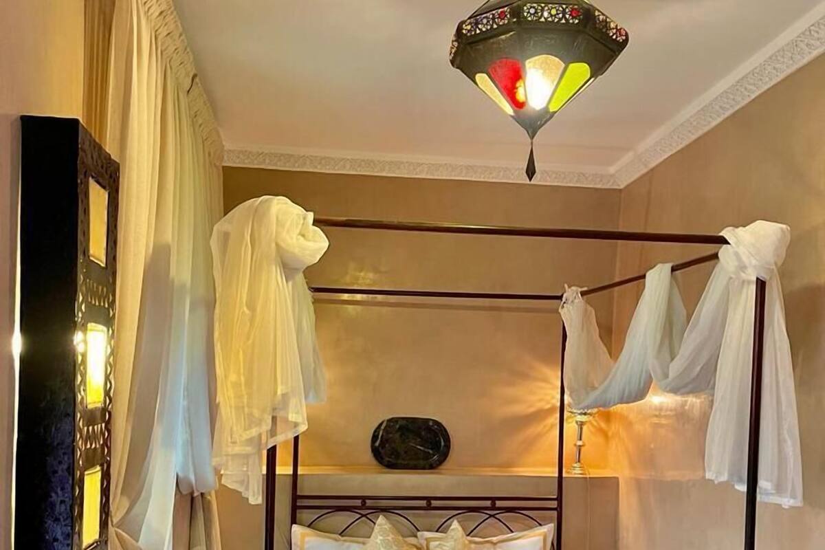 Una cama con dosel con sábanas blancas y almohadones decorativos, una lámpara colgante y un techo decorado.