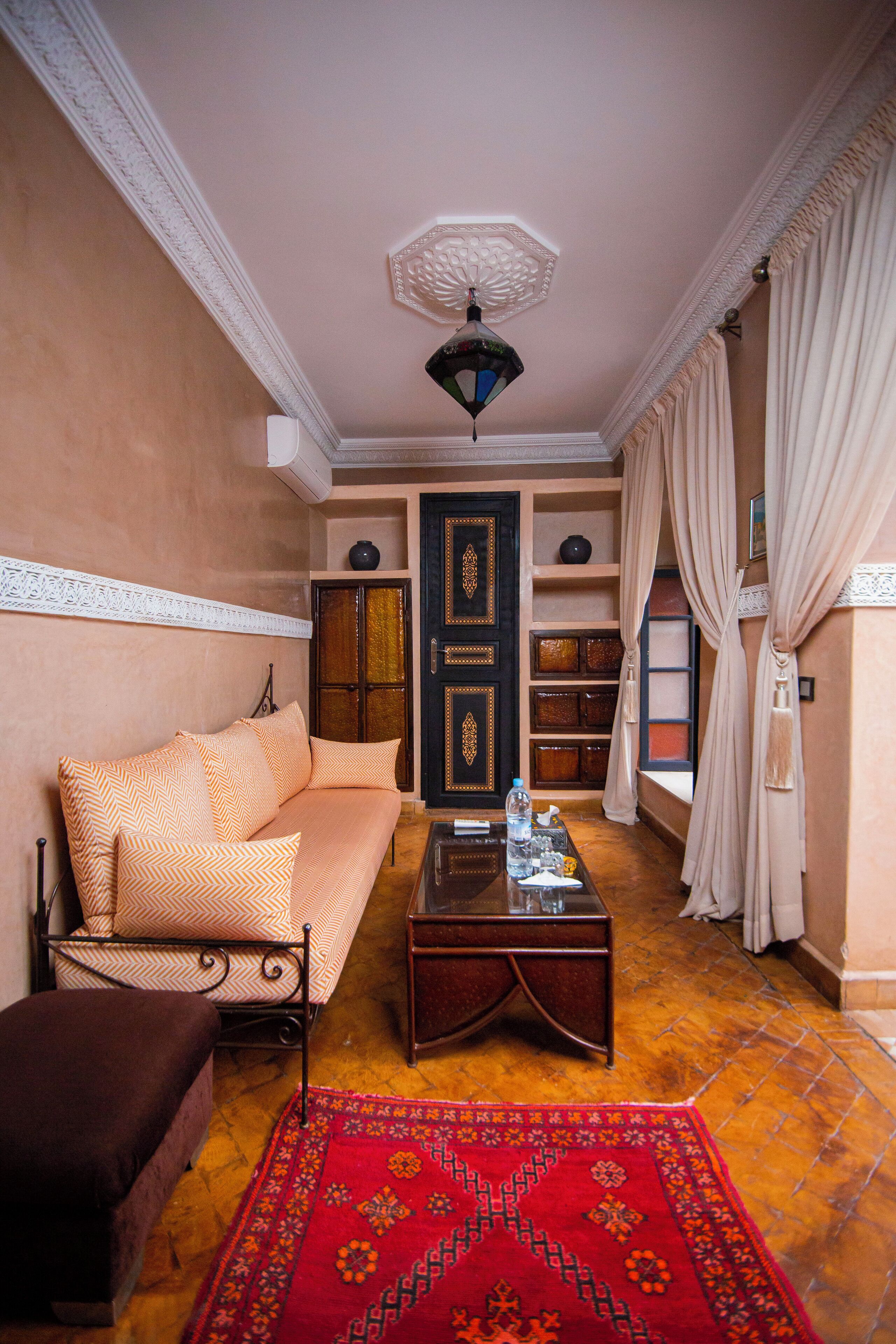A room with a sofa, a coffee table, a patterned rug, a decorative ceiling light, and a door with a traditional design.