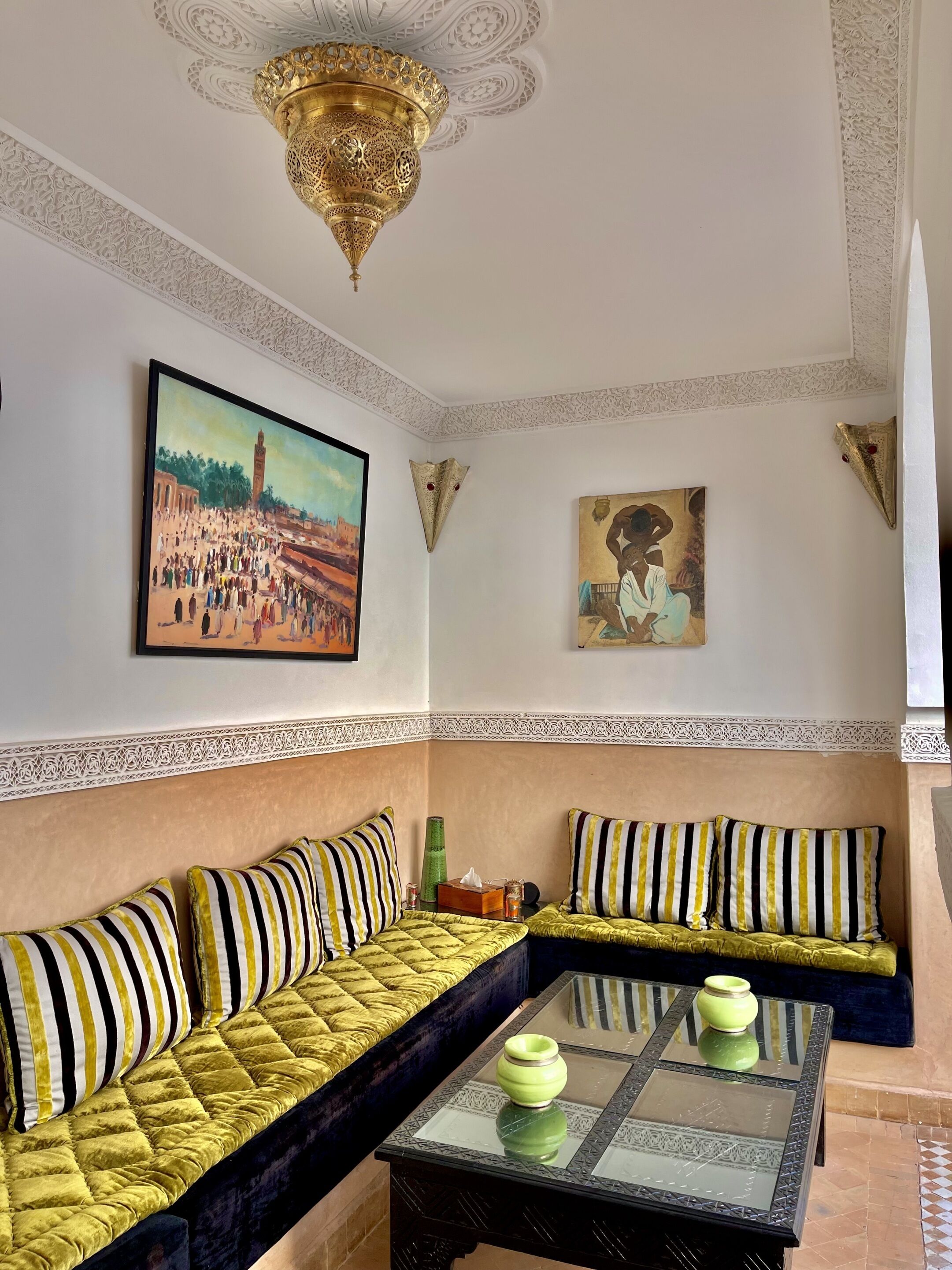 Een kamer met een zithoek, een tafel met glazen blad en twee schilderijen aan de muur.