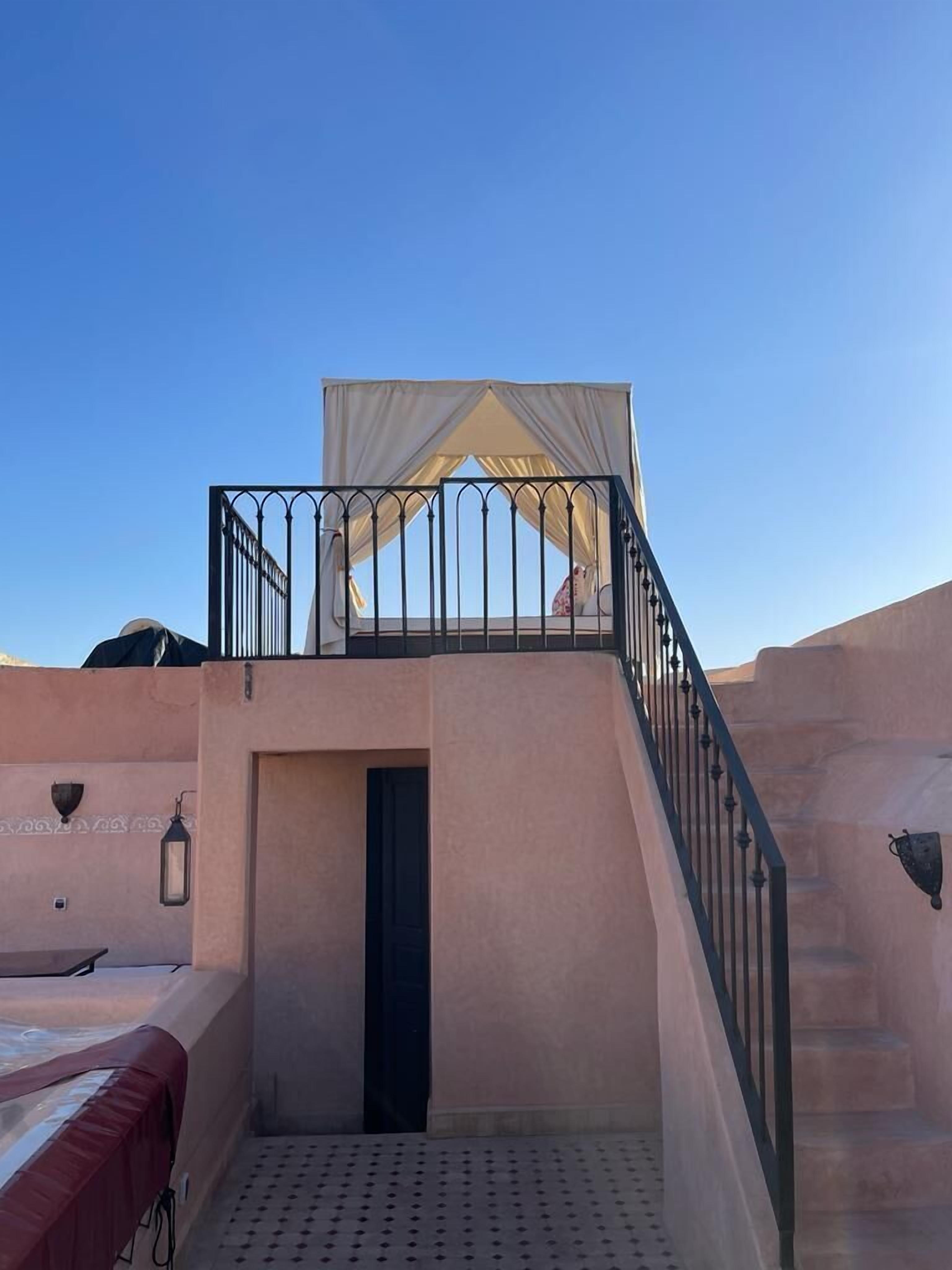Ein Balkon mit weißem Baldachin, einer Treppe und einem Bett mit roter Decke.