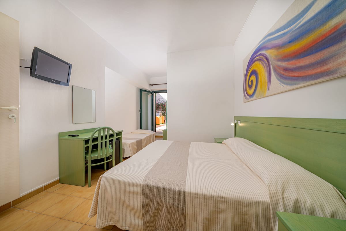 A hotel room with a bed, a desk, a chair, a television, and a painting on the wall.