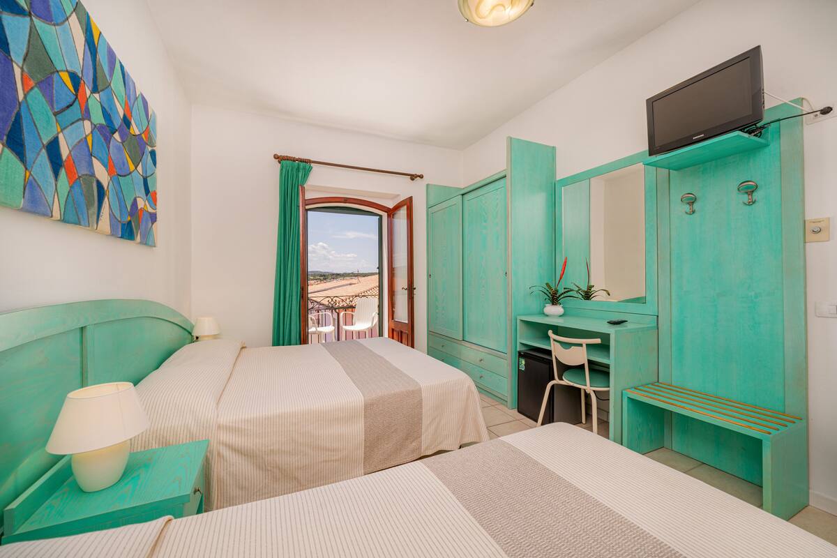 A bedroom with two beds, a desk, a TV, and a view of the outdoors.