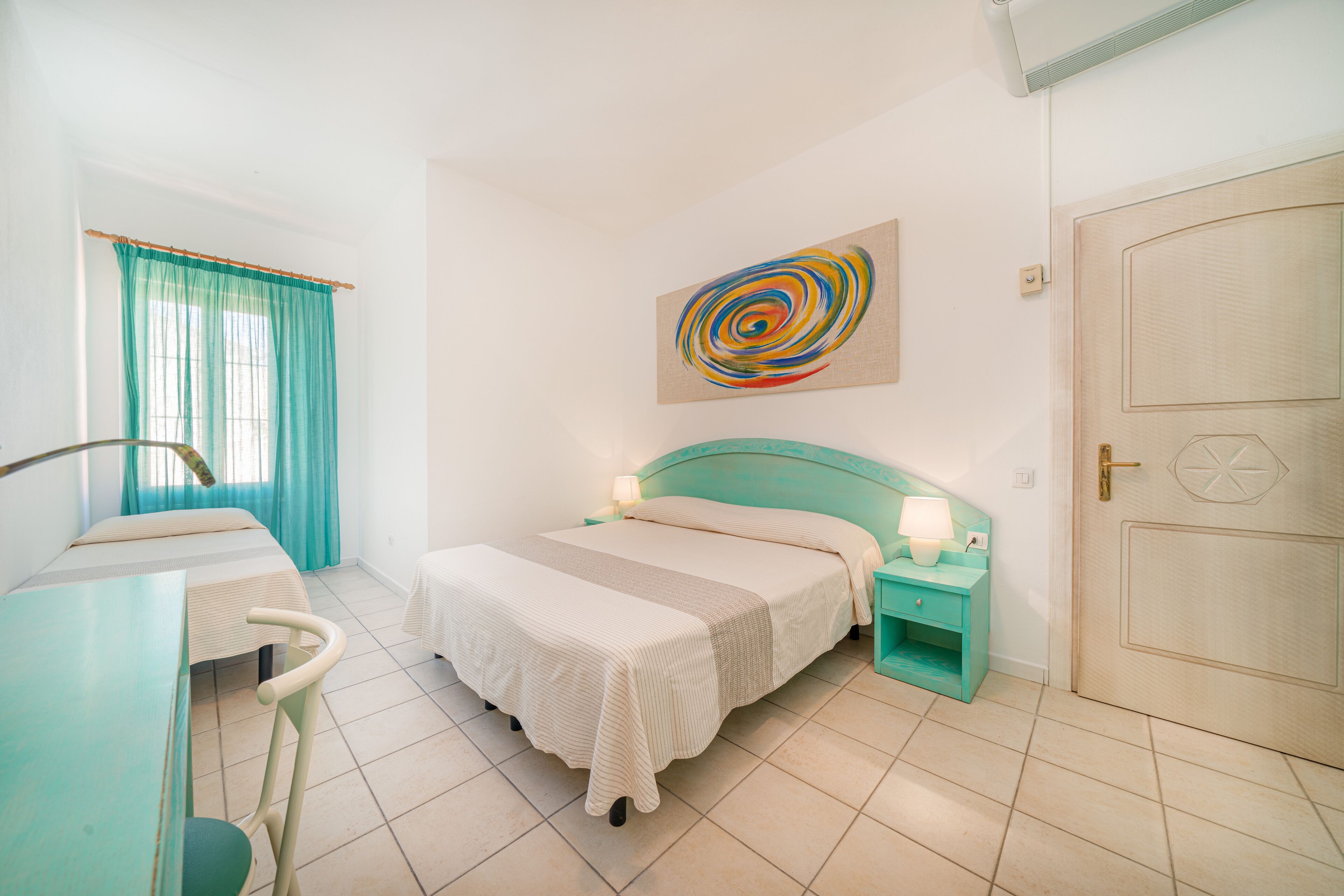 Un dormitorio con cama, escritorio, silla, mesita de noche y puerta.