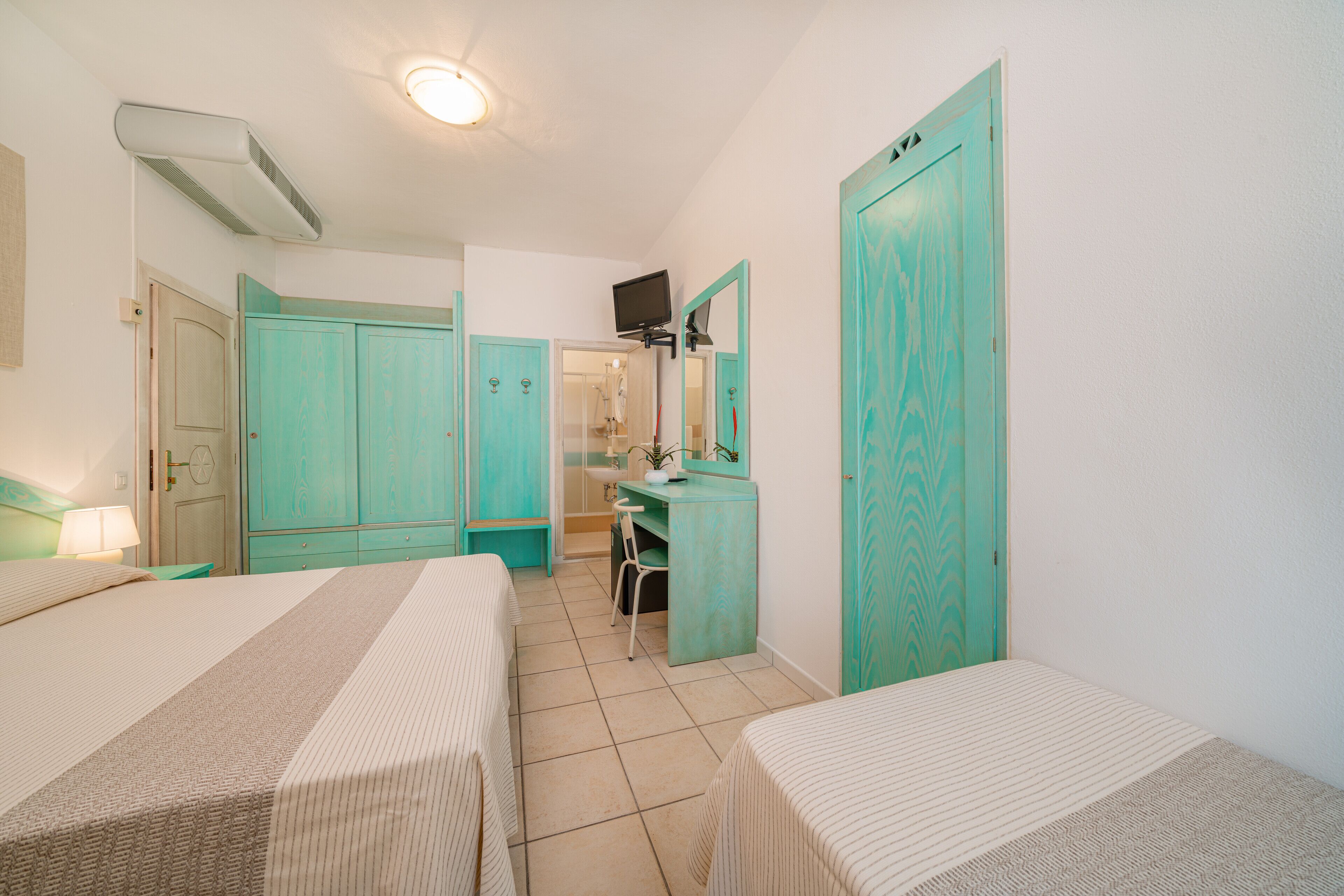 A room with two beds, a desk, a mirror, and a wardrobe.