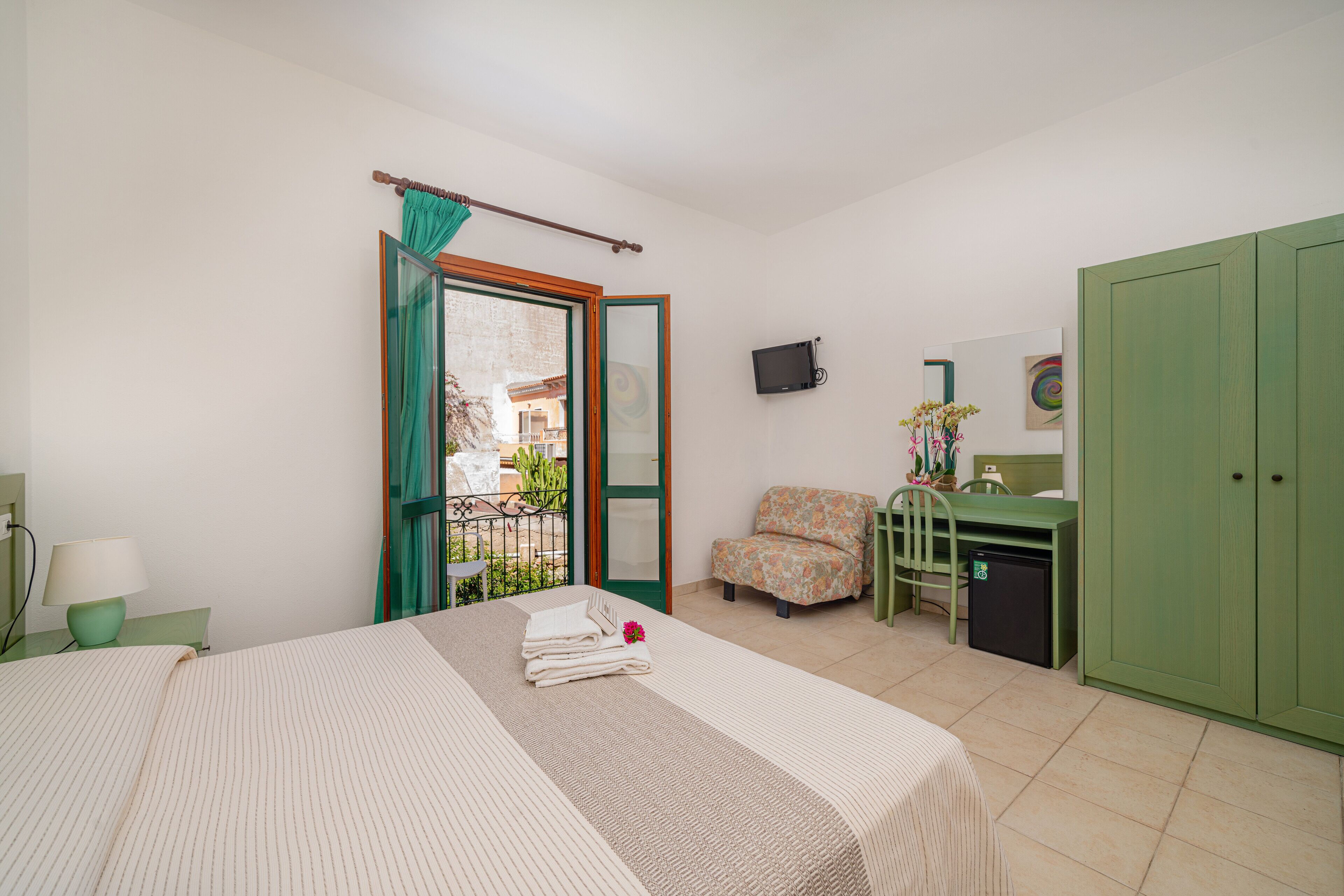 Habitación de hotel con cama, escritorio, silla, televisor y armario.
