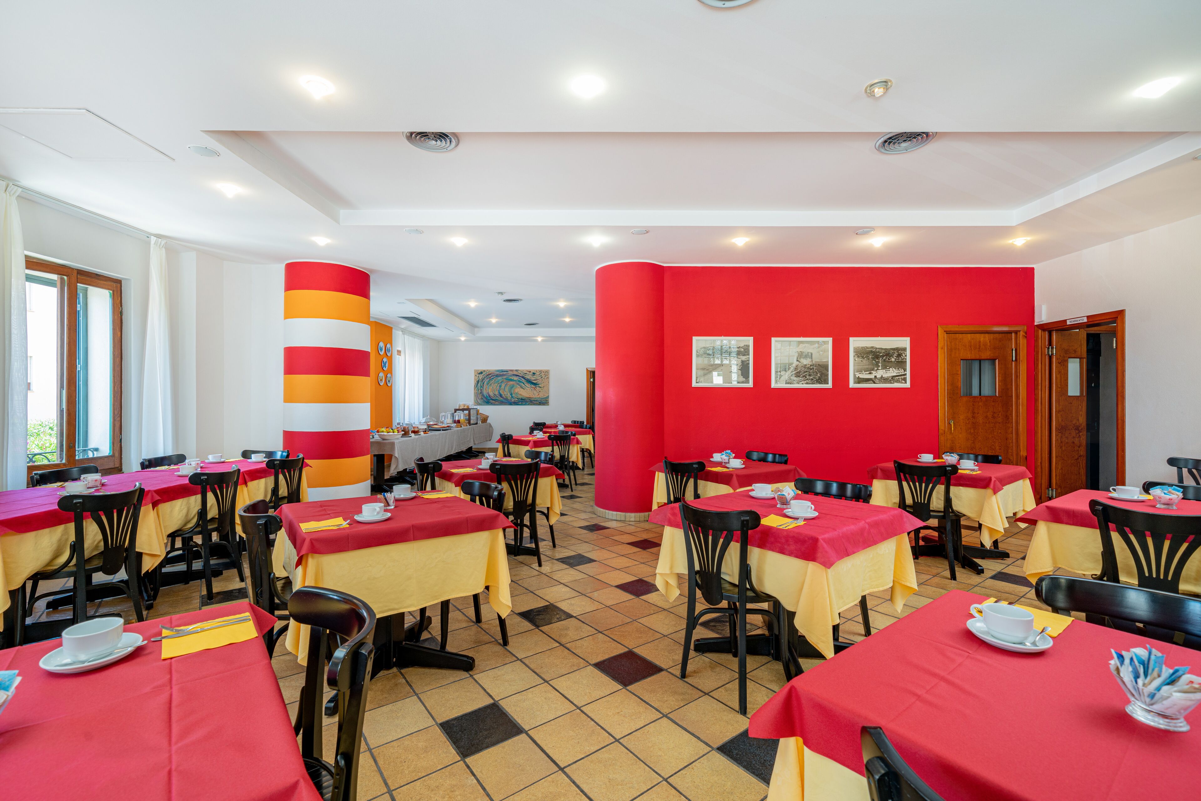 Un restaurante con manteles rojos y amarillos, sillas negras y piso de baldosas.