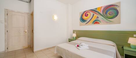 A hotel room with a bed, a green nightstand, a wall-mounted air conditioner, and a colorful abstract painting.
