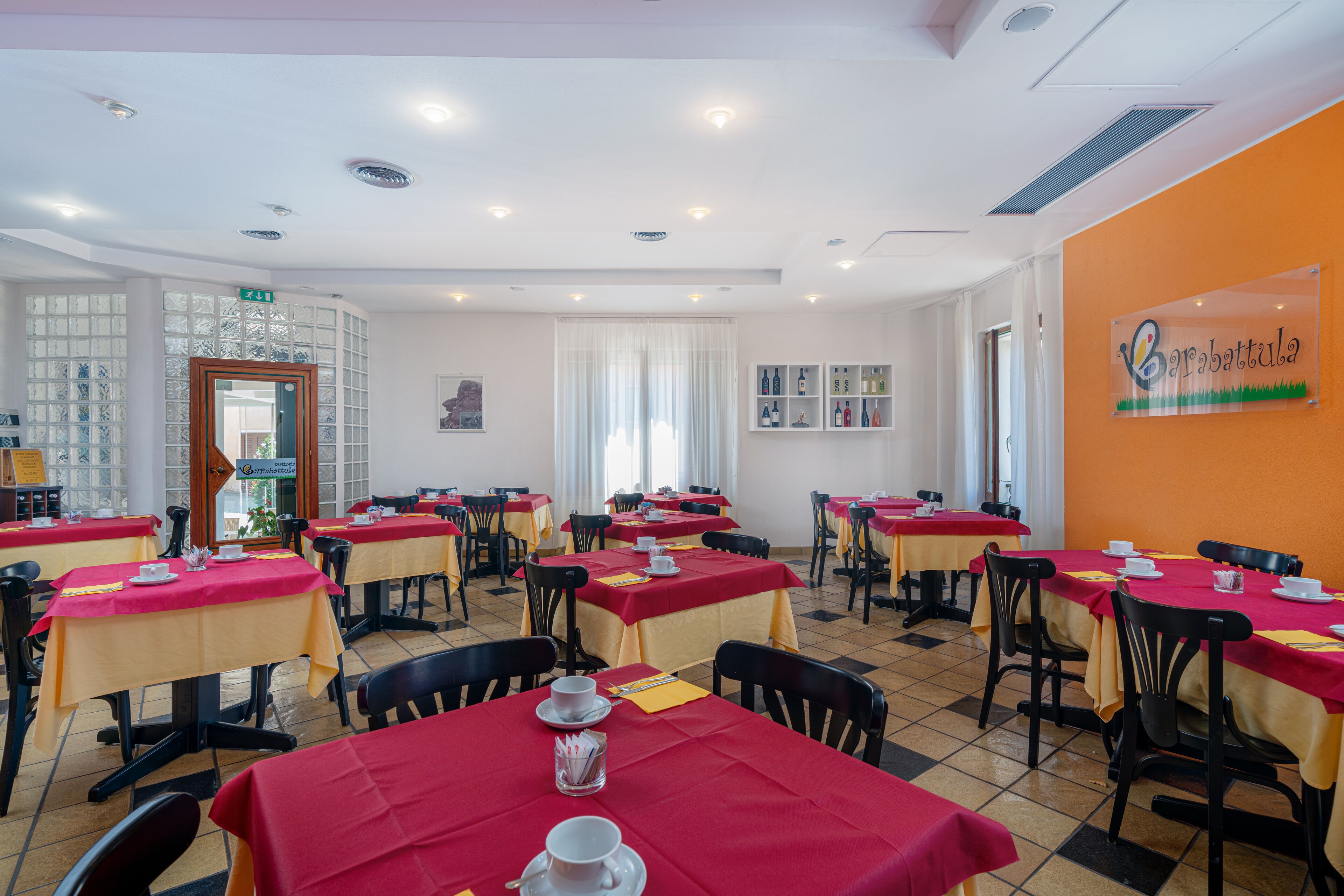 Un comedor con varias mesas, cada una cubierta con un mantel rojo y equipada con tazas y platillos blancos.