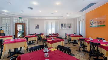 Un comedor con varias mesas, cada una cubierta con un mantel rojo y equipada con tazas y platillos blancos.