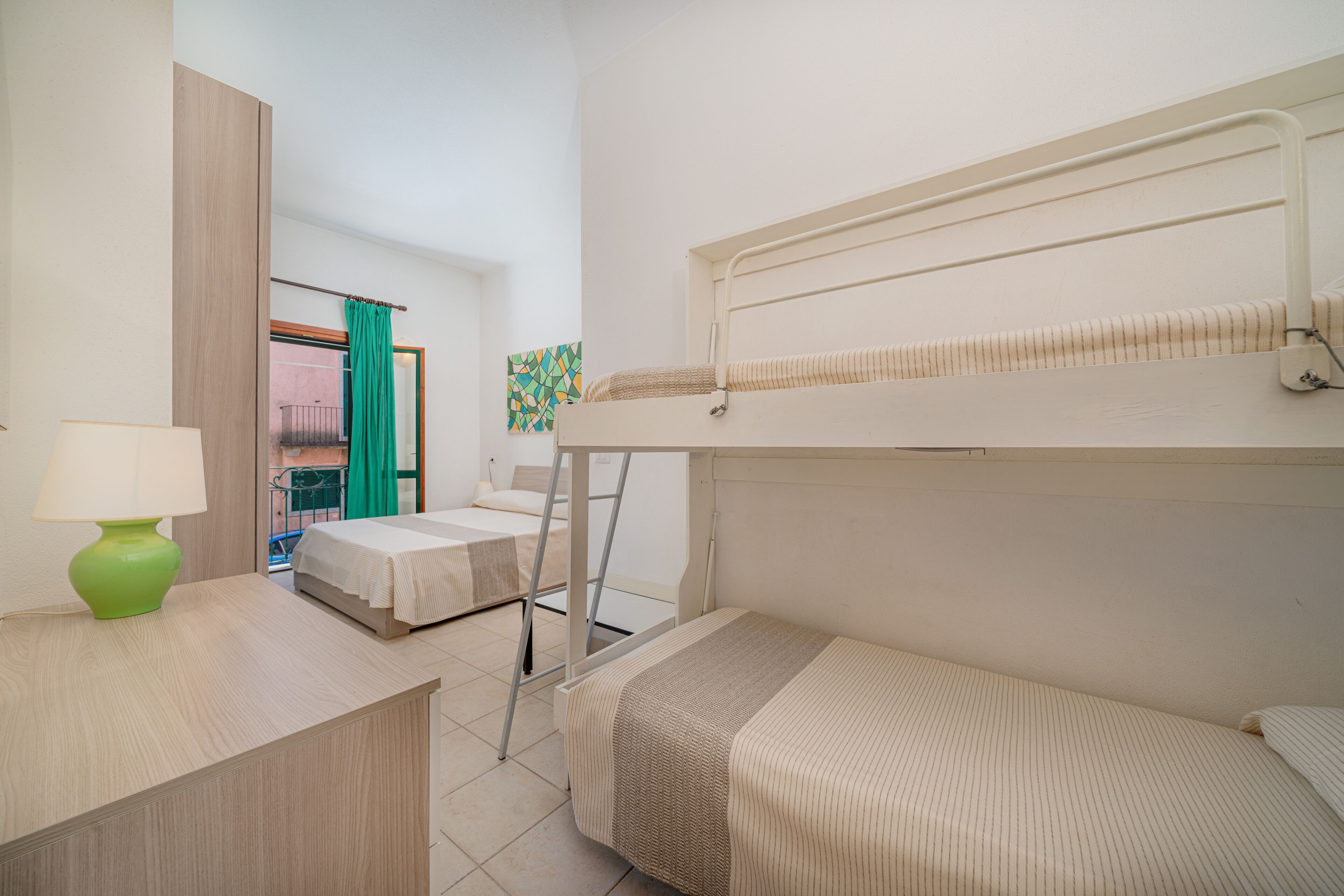 Une chambre d’hôtel compacte avec un lit superposé, un bureau avec une lampe et une vue sur le balcon extérieur.