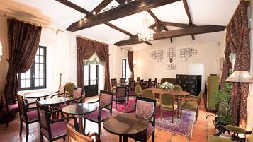 A dining area with round tables and chairs, a chandelier, and a patterned rug.