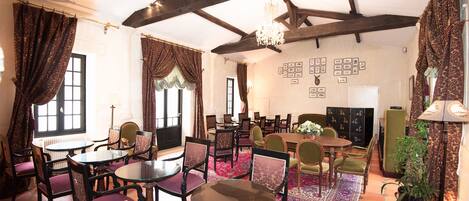 A dining area with round tables and chairs, a chandelier, and a patterned rug.