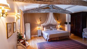 Un dormitorio con una cama grande, vigas de madera, dosel y una mesita de noche con lámpara.