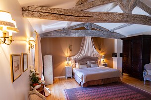 Un dormitorio con una cama grande, vigas de madera, dosel y una mesita de noche con lámpara.