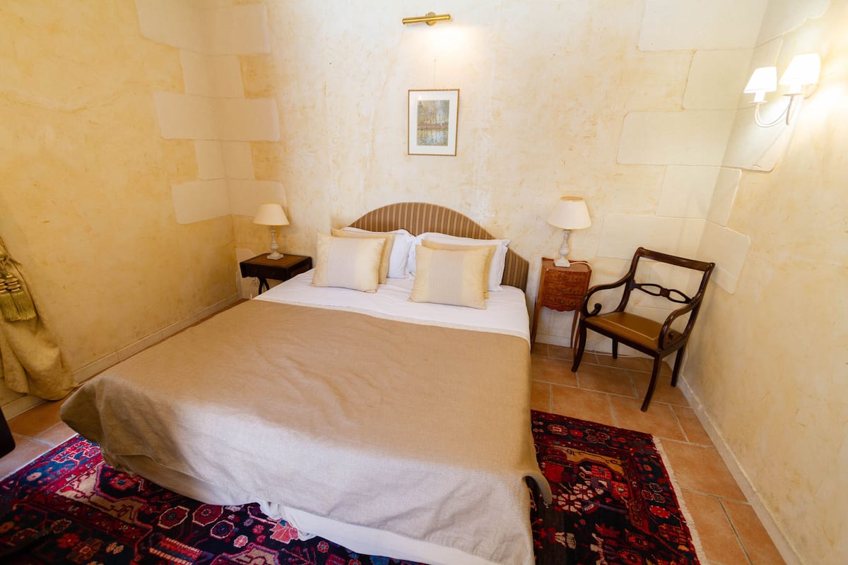Habitación de hotel ordenada con una cama grande, dos mesitas de noche con lámparas, una silla y una alfombra.