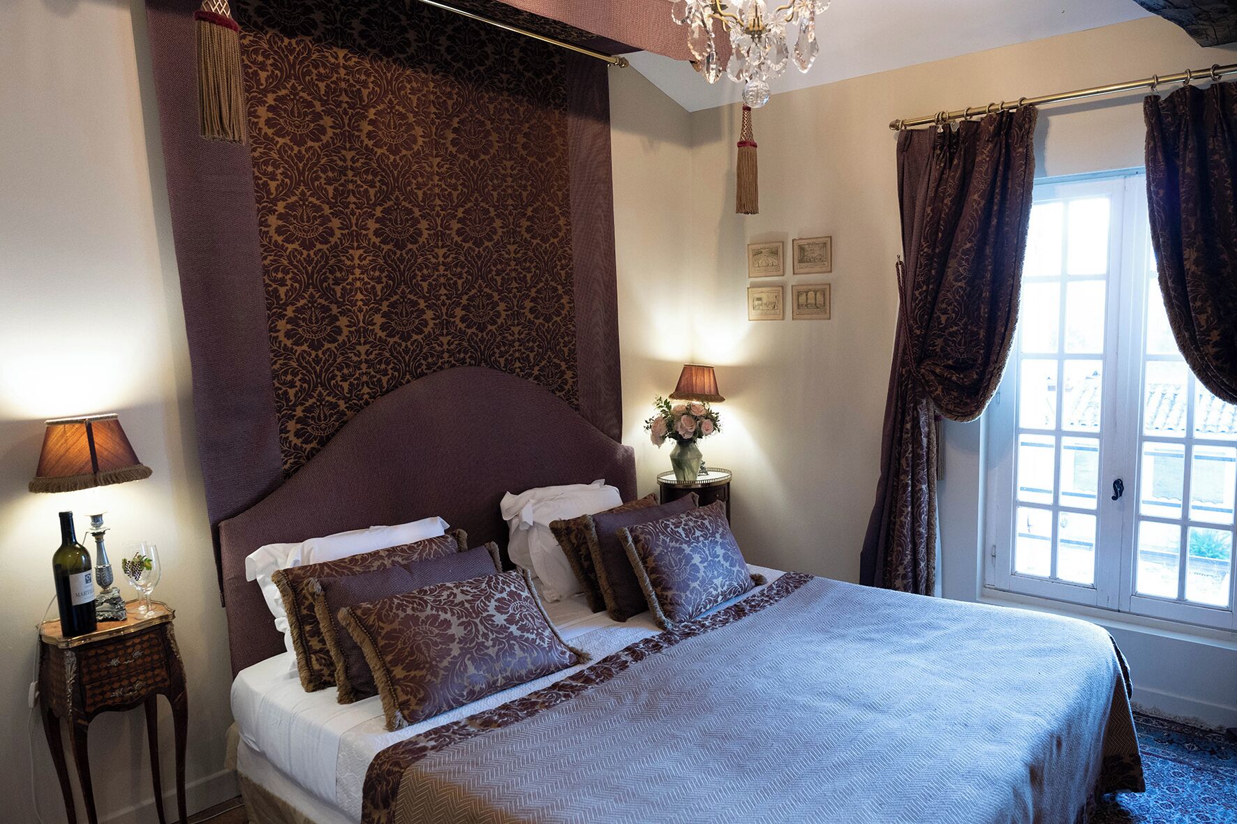 A bedroom with a large bed, patterned curtains, a chandelier, and a window with curtains.