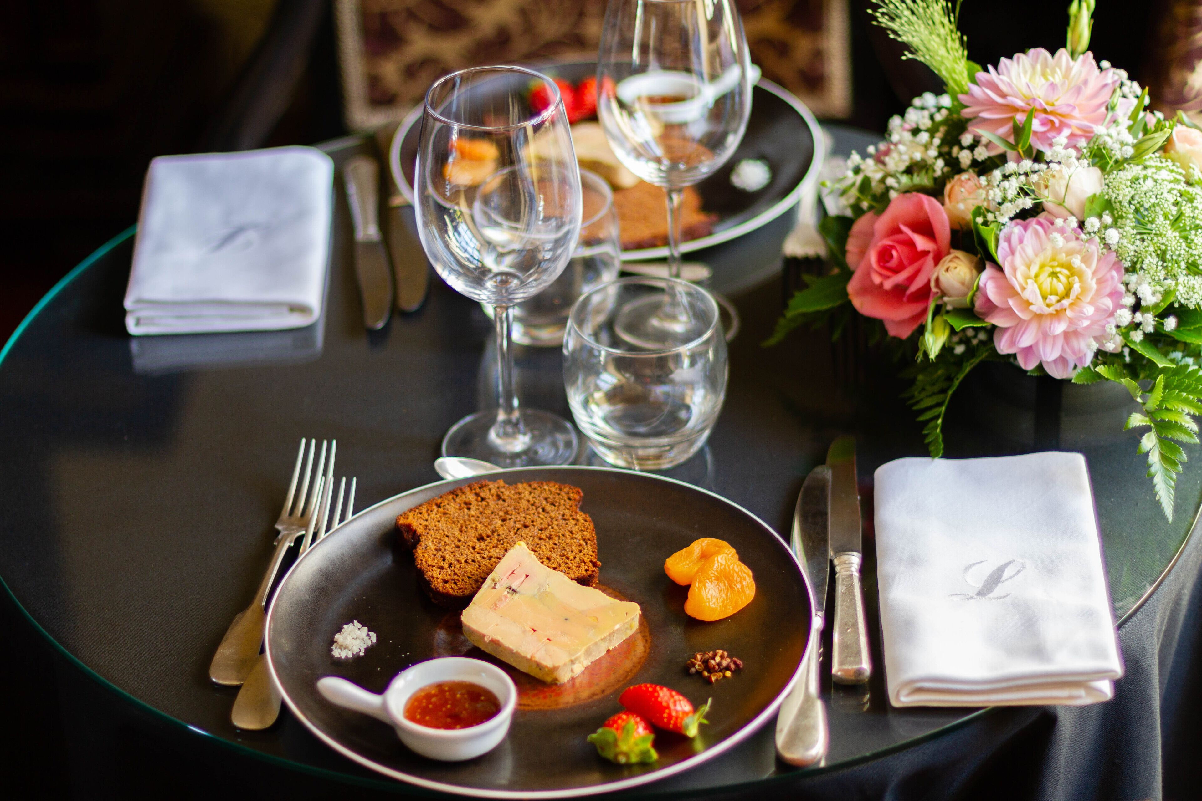 A dining table with a plate of food, a glass of water, and a vase of flowers.