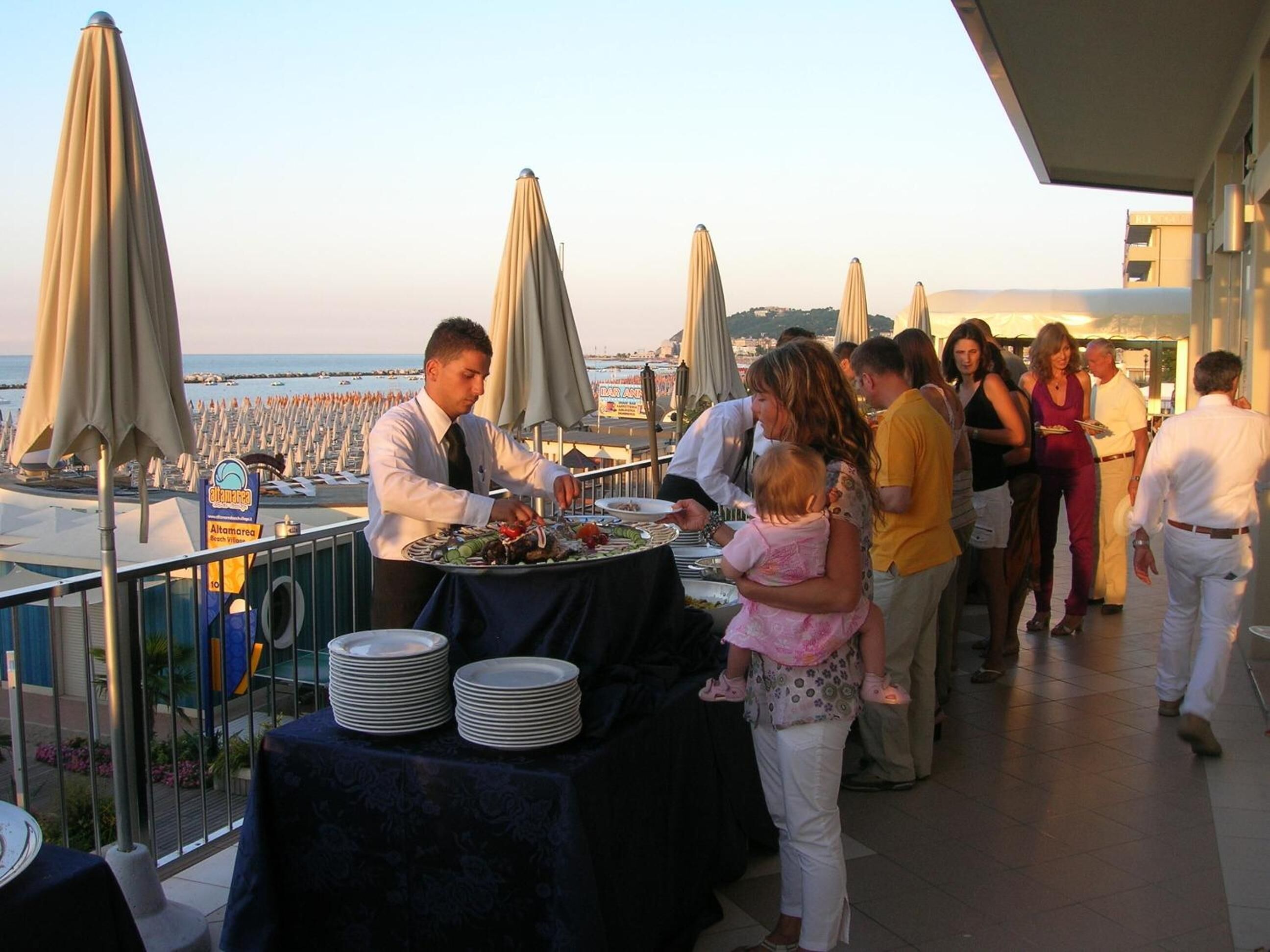 A terrace with a buffet setup, umbrellas, and a view of the sea.