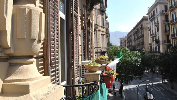 Fachada de edifício com grandes janelas, varandas e plantas em vasos.
