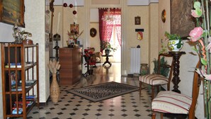 Quarto com chão xadrez, uma cadeira de madeira, uma estante e uma mesa com um vaso.