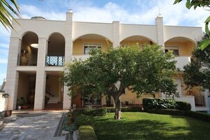 A two-story building with a symmetrical facade, arched windows, and a central tree in the courtyard.