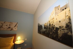 A bedroom with a bed, a nightstand, a lamp, and a large wall painting of a historical building.