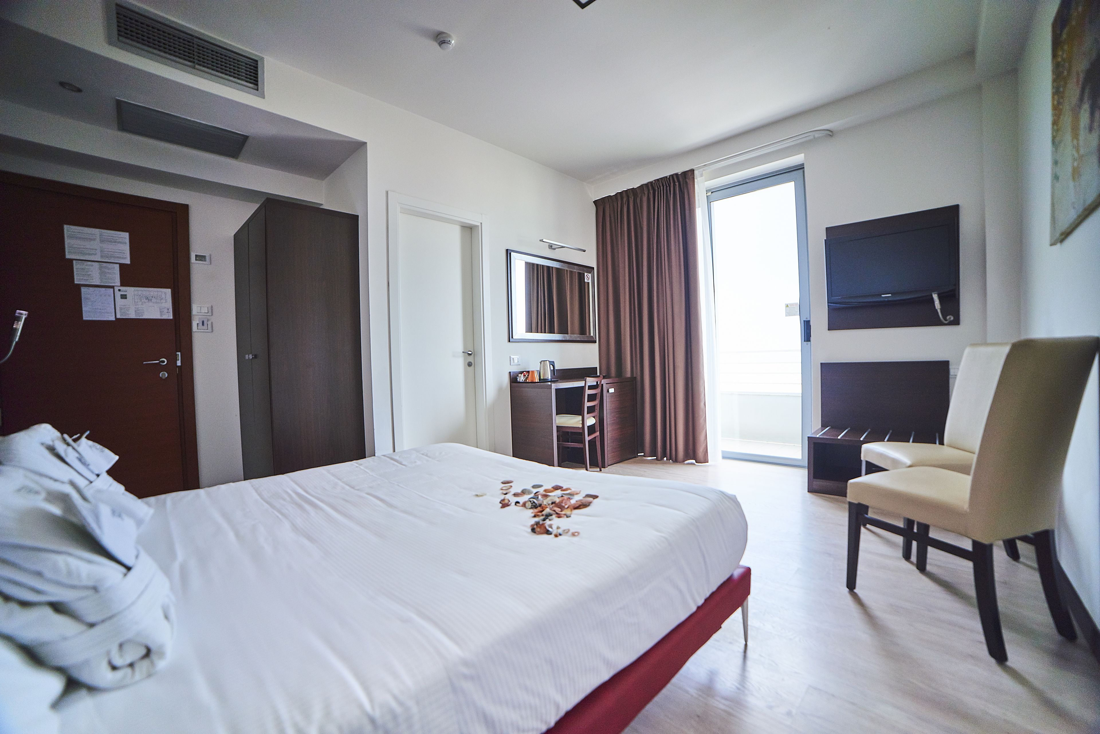 Ein Hotelzimmer mit Bett, Schreibtisch, Stuhl, Fernseher und einer Tür mit liegengebliebenen Papieren.