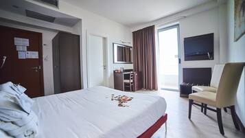 Ein Hotelzimmer mit Bett, Schreibtisch, Stuhl, Fernseher und einer Tür mit liegengebliebenen Papieren.