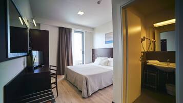 A hotel room with a bed, a desk, a TV, a bathroom with a sink and mirror, and a window with curtains.
