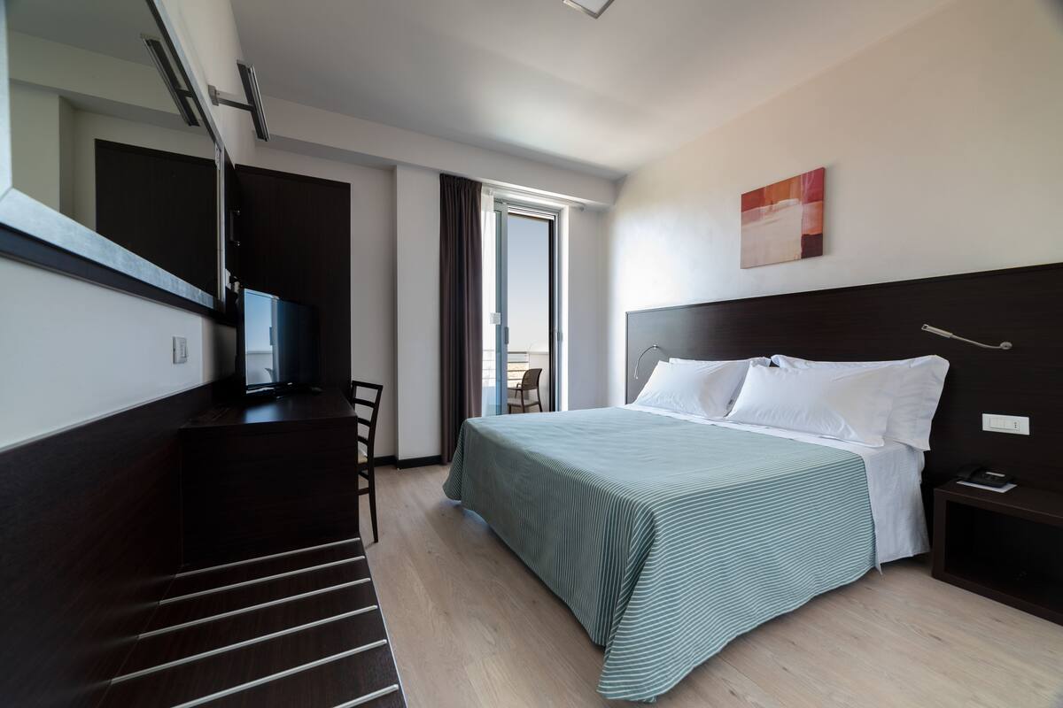 A hotel room with a bed, a desk, a chair, a television, and a window.