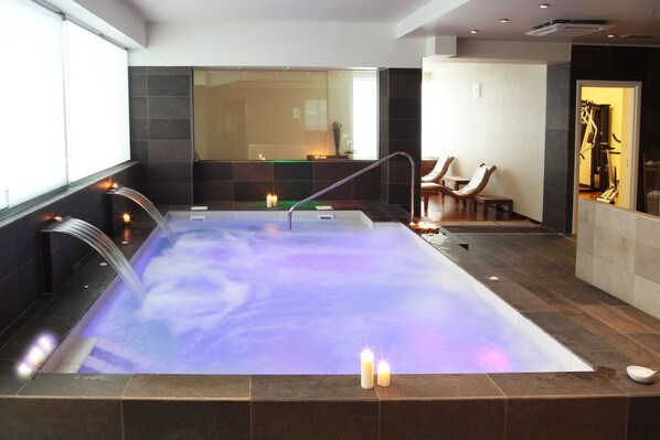 A modern spa with a large hot tub, a wooden bench, and candles. - Alisei Palace Hotel (Rimini)