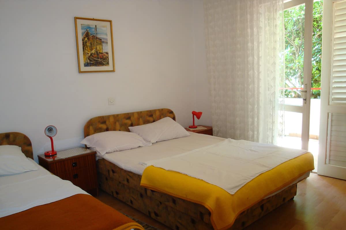 Una cama doble con una colcha amarilla, dos mesitas de noche con lámparas, un cuadro en la pared y una ventana con cortinas.