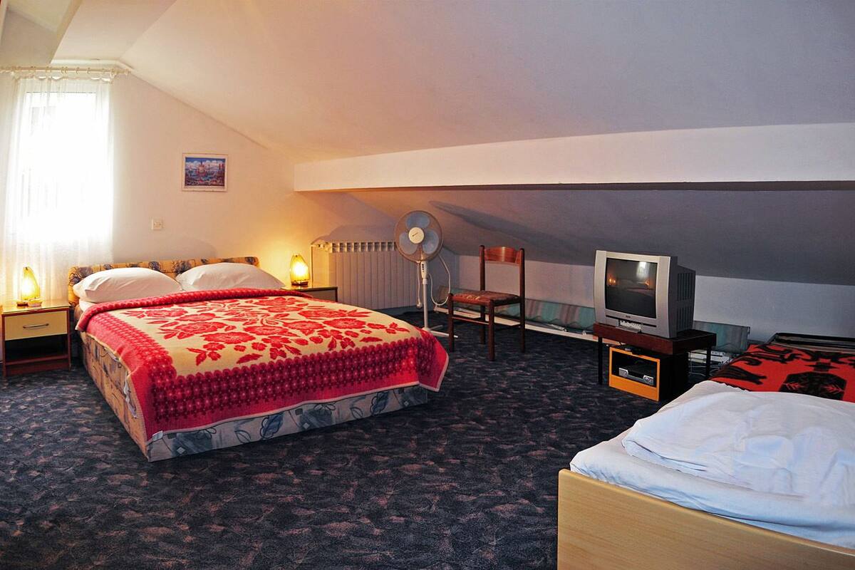 Habitación de hotel con cama, escritorio, silla, televisor y radiador.